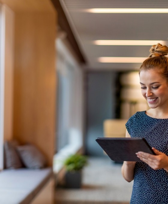 Eine junge Frau schaut lachend auf ihr Tablet. 