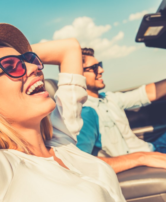 Eine Frau und  ein Mann sitzen zusammen im Cabrio und genießen das sonnige Wetter. 