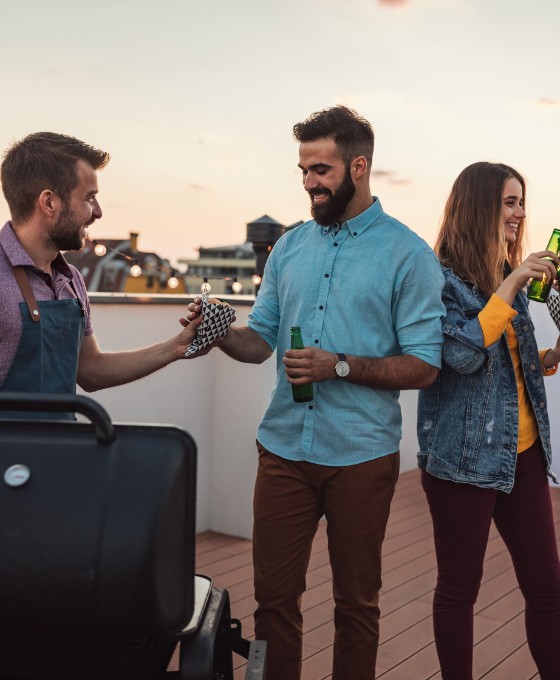 Eine Gruppe von Leuten grillt zusammen auf einer Dachterrasse. 