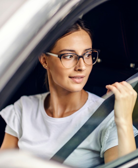Eine junge Frau schnallt sich an und blickt dabei aus dem Autofenster.