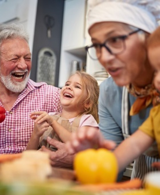 Großeltern kochen lachend gemeinsam mit ihren zwei kleinen Enkelkindern