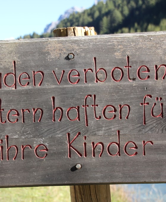 Ein Holzschild an einem See auf dem steht "Baden verboten. Eltern haften für ihre Kinder."