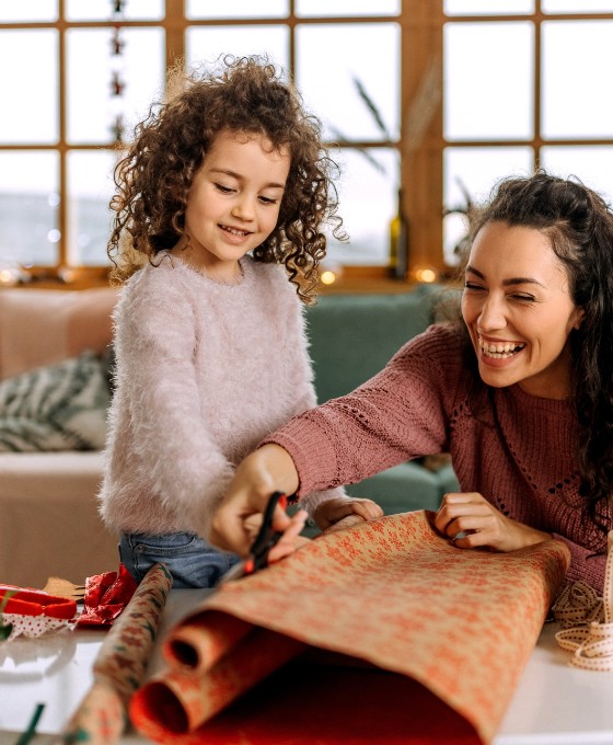 Eine Mutter packt mit ihrer kleinen Tochter Weihnachtsgeschenke ein. 