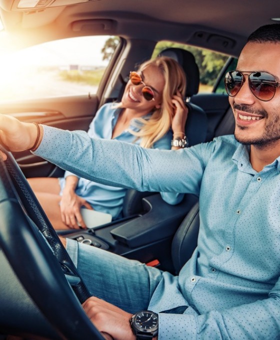 Ein Pärchen sitzt zusammen mit Sonnenbrille im Sonnenschein in einem Auto.