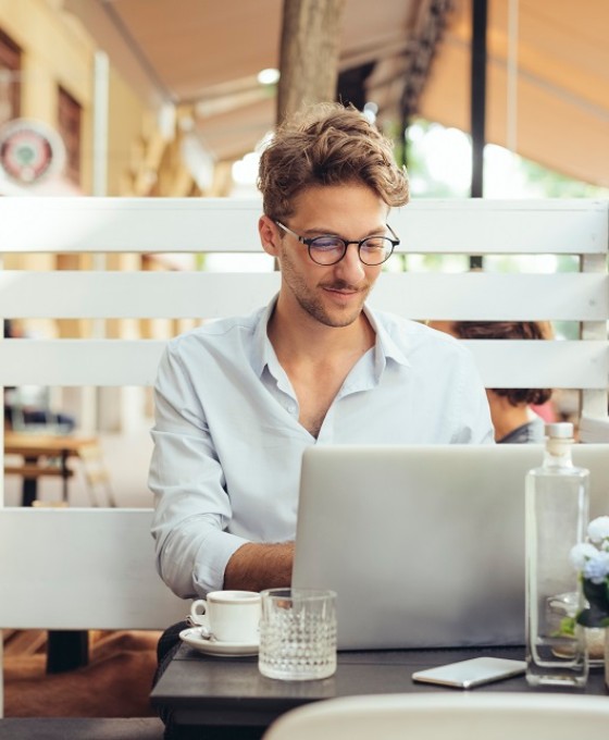 Ein junger Mann sitzt an seinem Laptop und einem Kaffee in einem Café. 