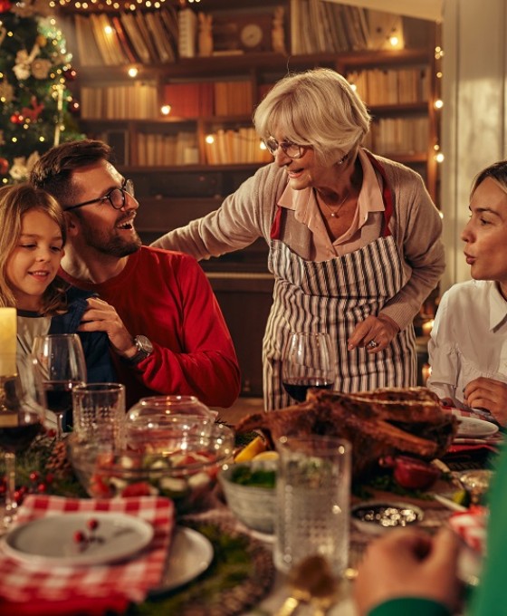 Eine Familie sitzt zusammen am Weihnachtstisch und isst. Drum herum ist es weihnachtlich geschmückt. 