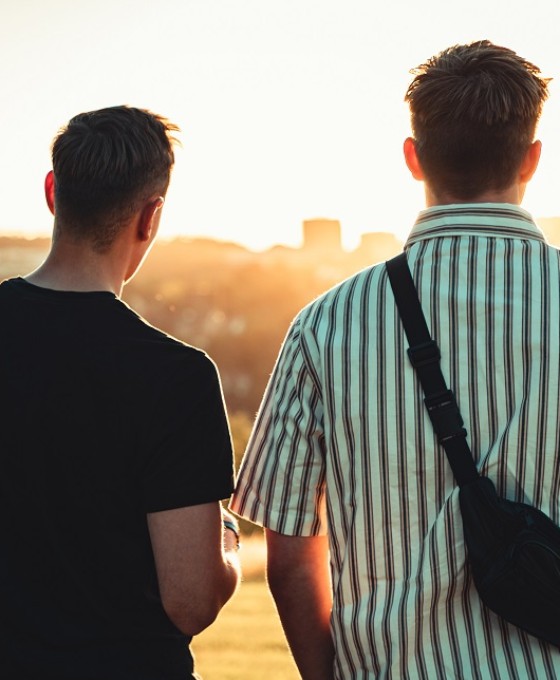 Zwei junge Männer stehen im Sonnenuntergang. Sie sind von hinten fotografiert.