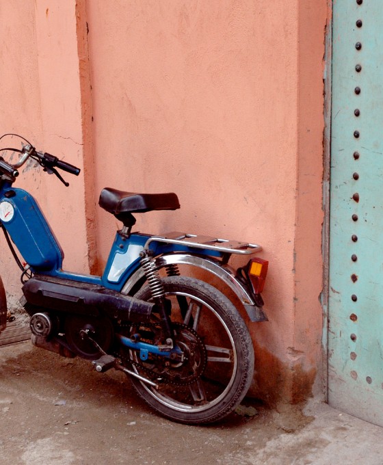 Das Bild zeigt ein älteres Moped, welches an einer Altbau-Hauswand gelehnt ist. 