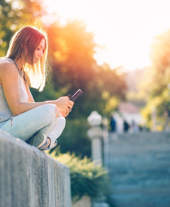 Ein Mädchen sitzt auf einer Steinmauer und schaut auf ihr Mobiltelefon. 