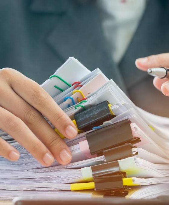 Zwei zusehende Hände gehen einen Stapel von gehefteten Dokumenten durch.