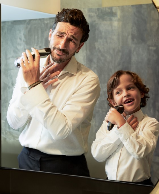 Vater und sein Sohn im Kindesalter stehen im Hemd vor einem Spiegel und rasieren sich im Gesicht