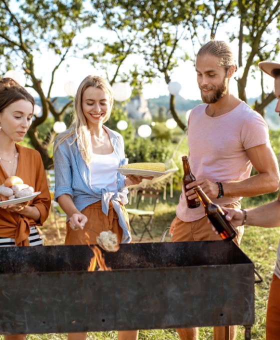 Eine Gruppe von Freunden steht zu viert an einem Holzgrill im Grünen. 