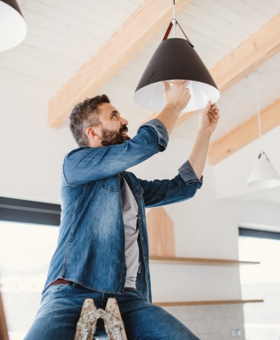 Ein Mann sitzt auf einer Leite und wechselt die Glühlampe einer Deckenleuchte. 