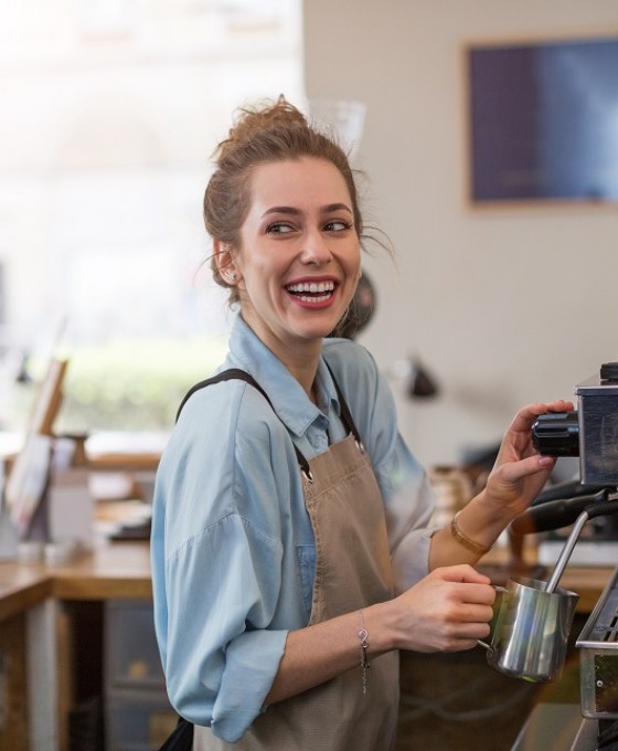 Eine junge Frau bereitet als Barista einen Kaffee an einer Kaffeemaschine in einem Café zu. 