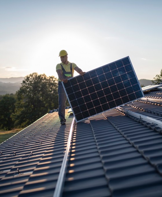 Ein Mann verlegt auf dem Dach eines Hauses Solarpanels.