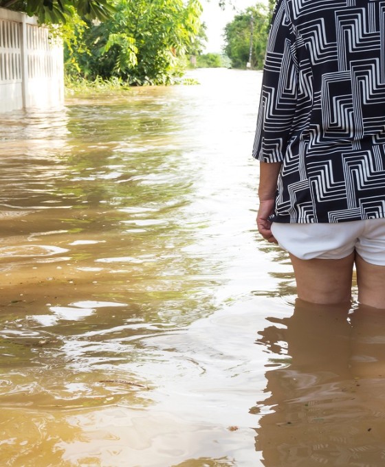 Eine Frau steht bis zu den Oberschenkeln im Wasser einer überschwemmten Straße.