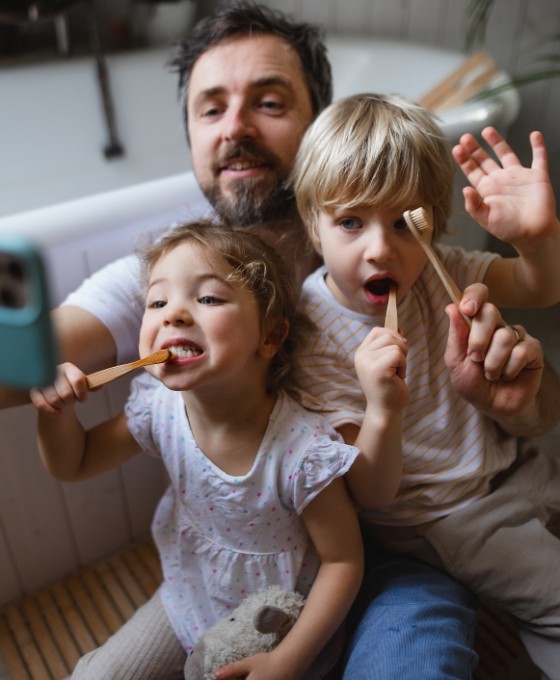 Ein Vater nimmt mit seiner Tochter und seinem Sohn ein Selfie auf, während sie beide am Zähne putzen sind.