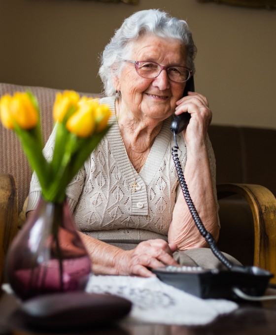 Eine ältere Dame sitzt in ihrem Zuhause am Kabeltelefon. 