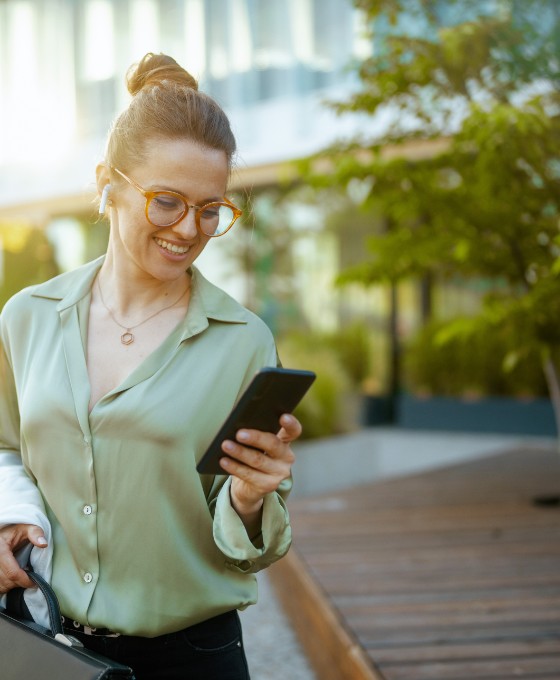 Eine junge Frau verlässt Bürogebäude und schaut glücklich auf ihr Telefon.