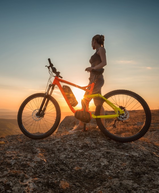 Eine Frau sitzt auf ihrem E-Bike auf einem Berg im Sonnenuntergang. 