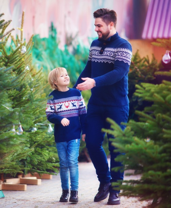 Ein junger Vater und sein Sohn suchen gemeinsam einen Weihnachtsbaum bei einem Verkauf aus.