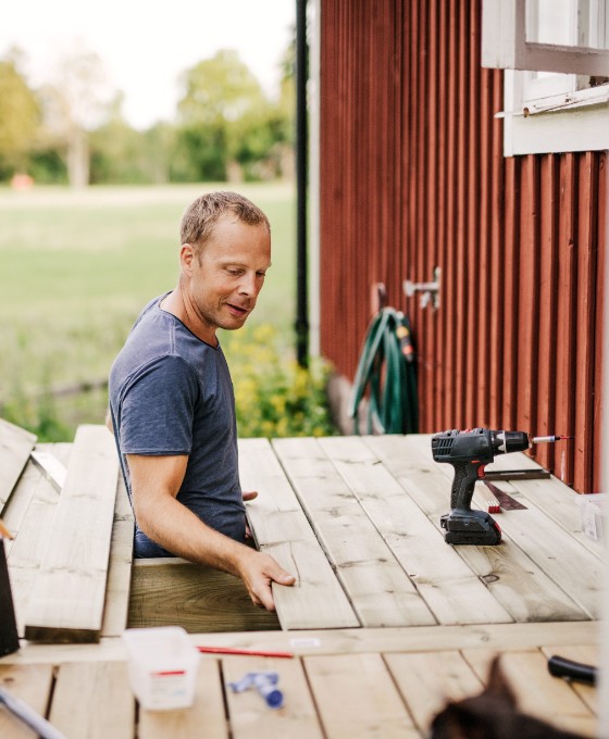 Ein Mann arbeitet an der Holzterrasse eines roten Schwedenhauses. 