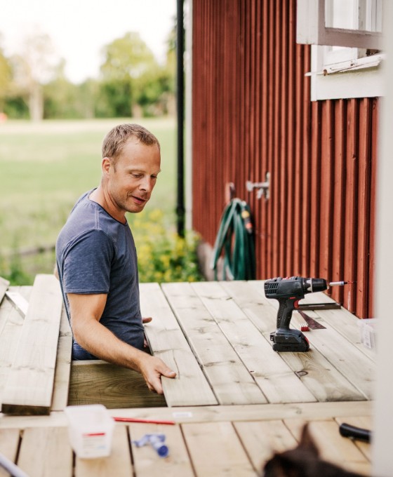 Ein Mann arbeitet an der Holzterrasse eines roten Schwedenhauses. 