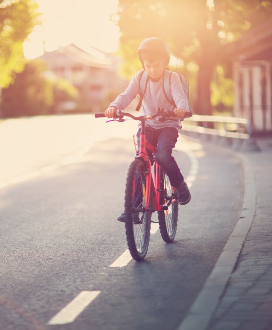 Ein junges Kind fährt mit seinem Fahrrad den Fahrradstreifen auf einer Straße entlang. 
