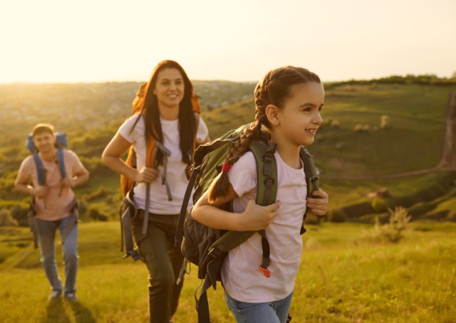 Eine junge Familie geht im Sonnenschein wandern. Die junge Tochter steht im Vordergrund.