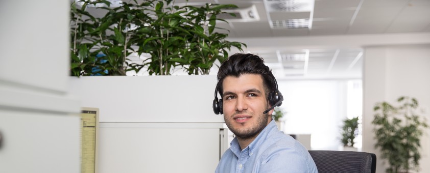 Ein Mann mit Headset sitzt an einem Schreibtisch.