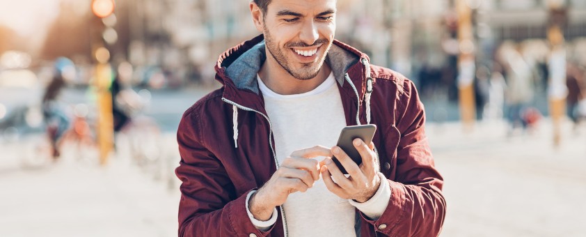 Ein junger Mann lächelt und tippt auf seinem Handy.