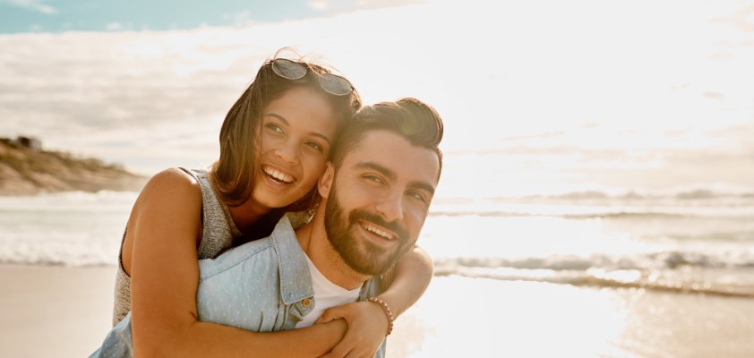 Ein junges Pärchen spaziert kuschelnd in der Sonne am Strand