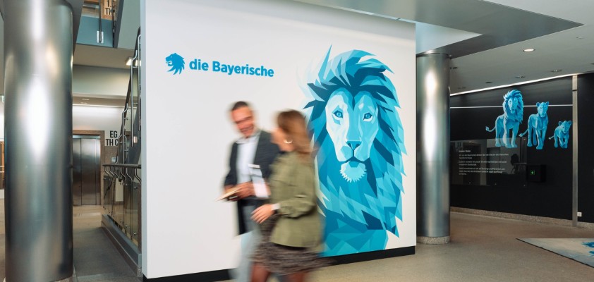 Eine Mitarbeiterin und ein Mitarbeiter der Bayerischen laufen gemeinsam durchs Foyer der Bayerischen
