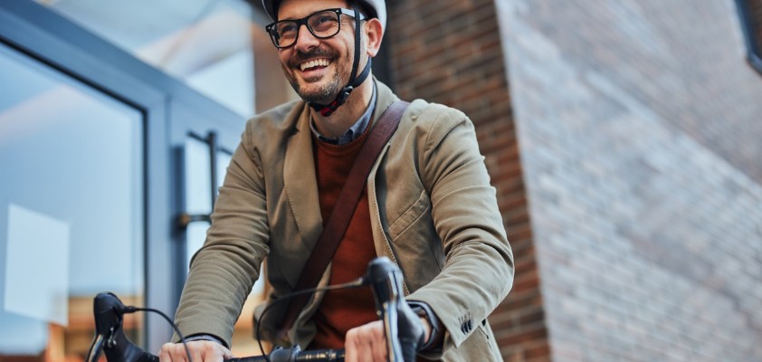 Ein Mann im Sacko mit Helm fährt mit seinem Fahrrad los.