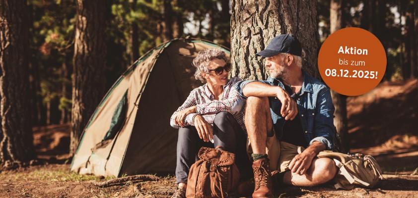 Eine Frau ein Mann in Wanderkleidung sitzen nebeneinander angelehnt an einen Baum und unterhalten sich. Hinweis im Bild: Aktion bis zum 08.12.2025
