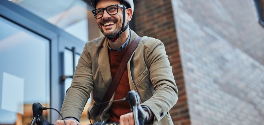 Ein Mann im Sacko mit Helm fährt mit seinem Fahrrad los.