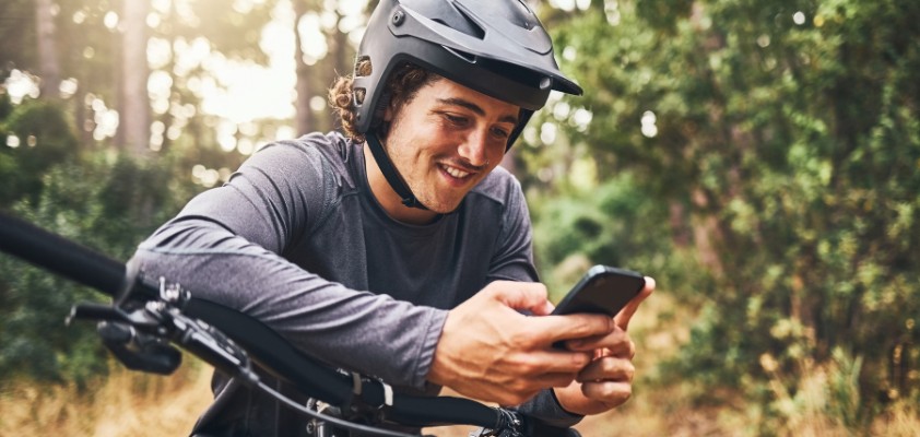 Junger Mann mit Helm und Smartphone auf seinem Mountainbike in der Natur