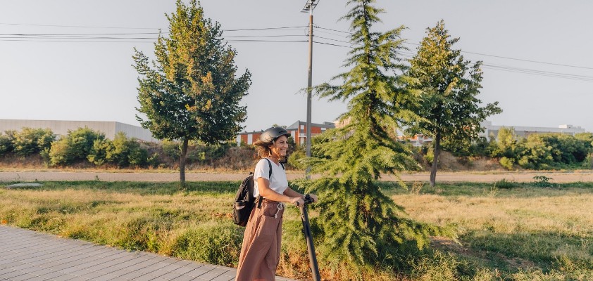 Junge Frau mit Helm fährt auf einem E-Scooter durch eine Grünanlage.