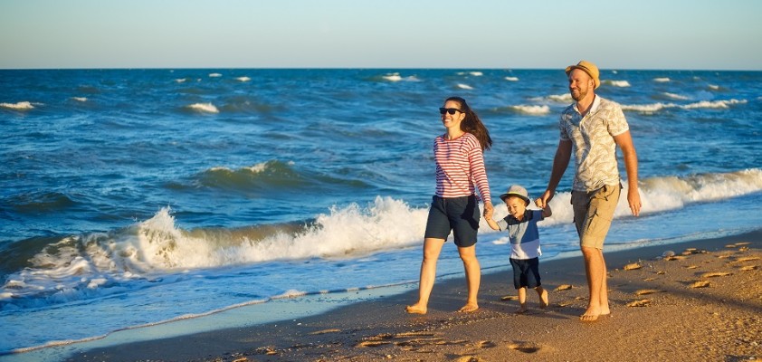 Ein Pärchen läuft mit ihrem Kleinkind Hand in Hand einen Strand entlang. 