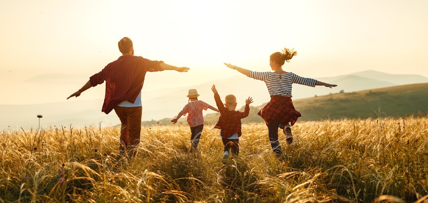 Familie läuft durch ein Feld bei Sonnenuntergang, Arme ausgestreckt in Freude.