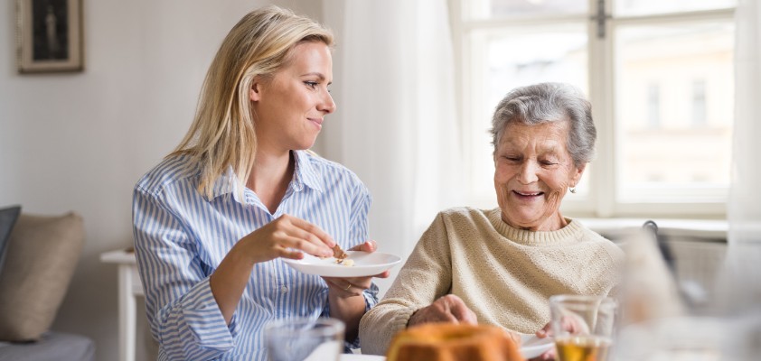 Eine erwachsene und eine ältere Frau sitzen zusammen für Tee und Kuchen. 