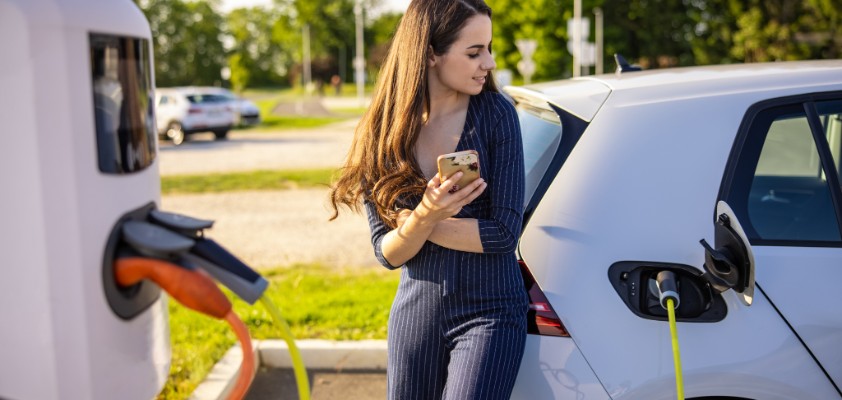 Eine junge Frau wartet bis ihr Elektroauto aufgeladen ist.