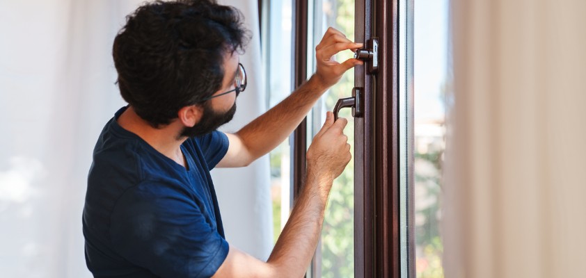 Ein Mann verschließt ein Fenster und trifft Vorkehrungen gegen einen Einbruch.