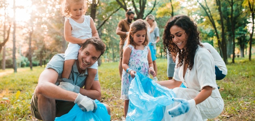 Eine junge Familie sammelt gemeinsam Müll im Grünen.