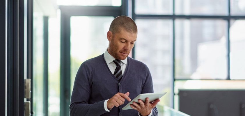 Ein Mann mit Krawatte steht im Büro und tippt auf seinem Tablet