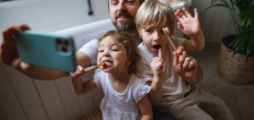 Ein Vater nimmt mit seiner Tochter und seinem Sohn ein Selfie auf, während sie beide am Zähne putzen sind.