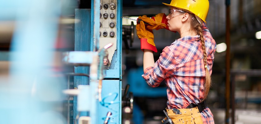 Eine junge Handwerkerin schraubt an einer Maschine. 