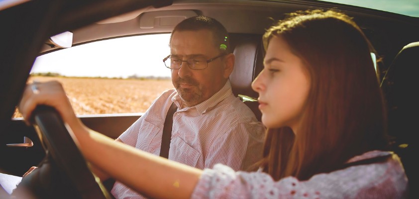 Ein junges Mädchen und ein erwachsener Mann sitzen zusammen in einem Auto. Das junge Mädchen sitzt am Steuer und lernt das Autofahren.