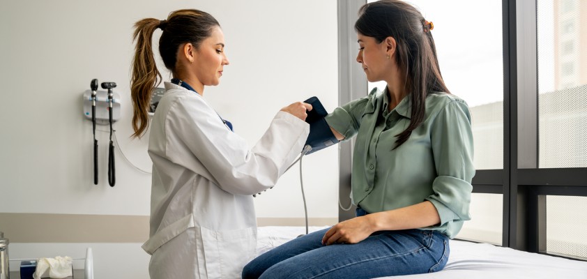 Ärztin misst einer Patientin den Blutdruck in einem Behandlungsraum.