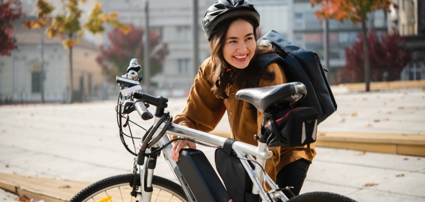 Eine junge Frau mit Rucksack und Fahrradhelm hockt vor ihrem E-Bike.